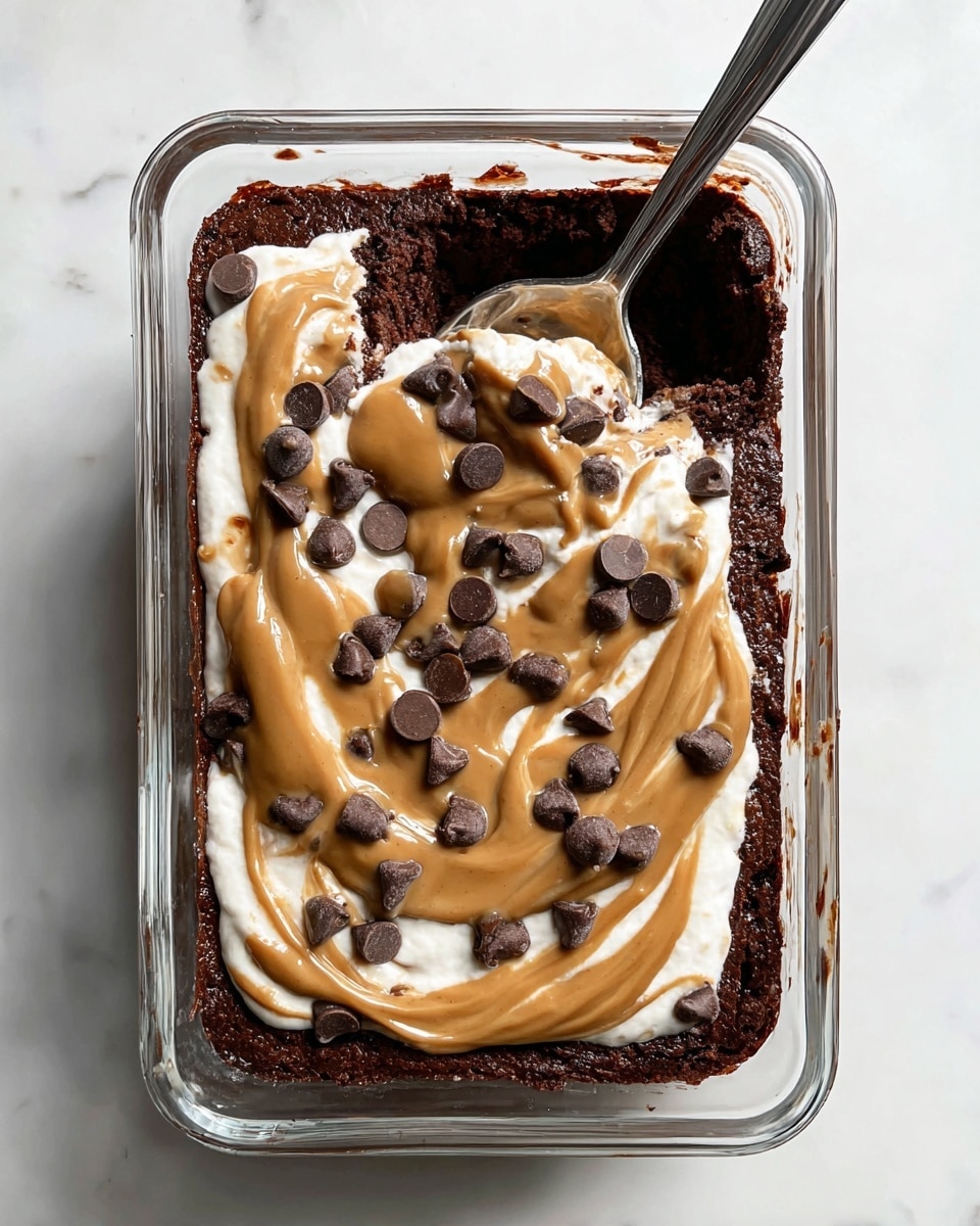 A rectangular glass dish holds a rich dark brown chocolate base layer with a moist texture. On top, there is a creamy white layer, partially covered by a smooth, light brown peanut butter drizzle that starts near the top center and flows downward. Scattered on the top are several dark chocolate chips, some lying flat and others standing on their ends. A silver spoon is stuck into the dessert on the right side, slightly pressing into the layers and lifting a bit of the peanut butter and white cream. The dish is set on a white marbled surface. photo taken with an iphone --ar 4:5 --v 7