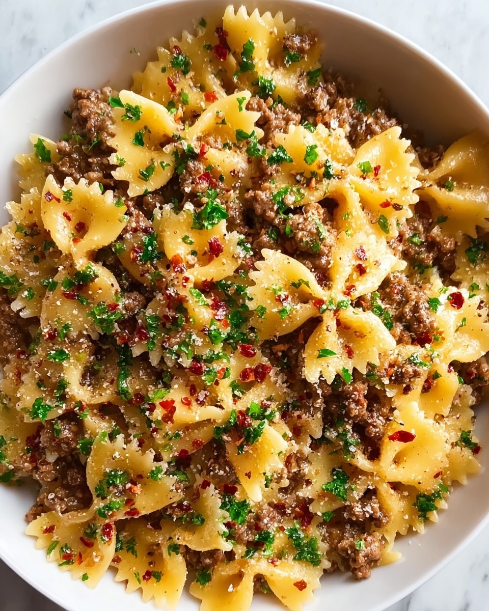 A close-up view of a white bowl filled with farfalle pasta mixed with crumbled cooked ground meat, giving a textured and hearty look with brown and yellow tones. The pasta is coated lightly with a glossy sauce and sprinkled with finely chopped green parsley and small red chili flakes, adding bright spots of color. There are small bits of grated cheese scattered evenly across the dish, creating a slightly grainy surface on some pasta pieces. The bowl sits on a white marbled surface. photo taken with an iphone --ar 4:5 --v 7