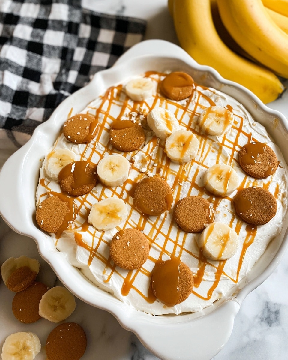 A close-up view of a dessert in a white dish with scalloped edges, showing a thick white creamy layer topped with a grid of caramel drizzles. On top, there are round golden-brown cookies and circular banana slices evenly spread across the surface. The dish is set on a white marbled surface with a black and white checkered item and a bunch of yellow bananas nearby. photo taken with an iphone --ar 4:5 --v 7