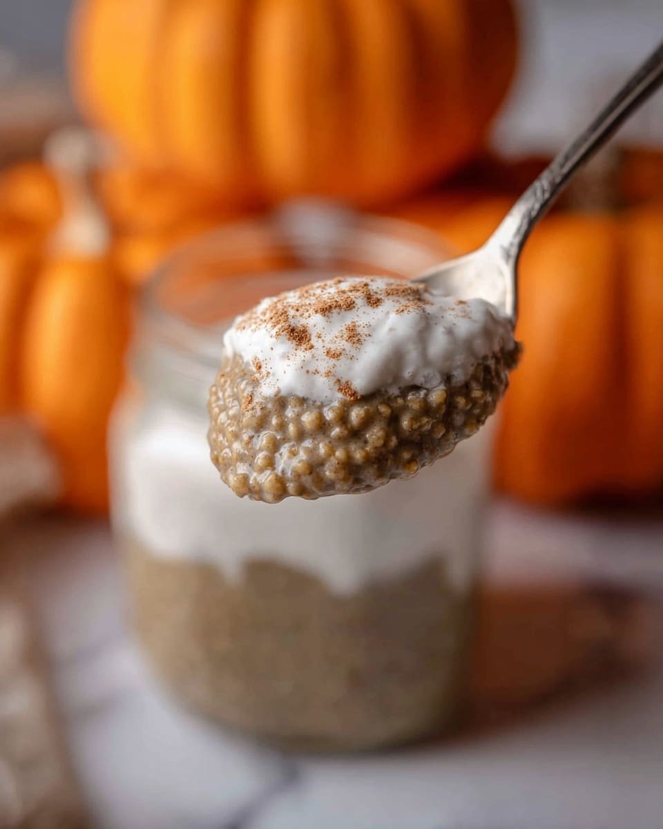 A close-up of a spoon holding a layered mixture with a dense, grainy brown bottom layer and a smooth, white creamy top layer, slightly dusted with a brown powder, with the spoon positioned in front of a blurred glass jar filled with a similar mixture and bright orange pumpkins in the soft background, all placed on a white marbled surface. photo taken with an iphone --ar 4:5 --v 7