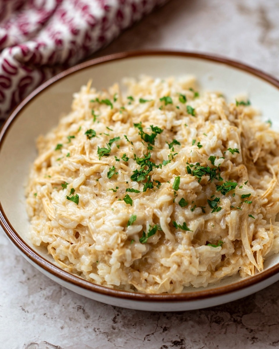 A clear glass baking dish filled with a creamy, baked rice casserole showing one scoop lifted on a wooden spoon in the foreground. The casserole has two visible layers: the top layer is pale golden with toasted cheese and herbs sprinkled evenly, creating a slightly crunchy texture, and the bottom layer is a moist mix of white rice and shredded chicken with small bits of mushrooms, visible as light and darker tones mixed gently. The dish rests on a white marbled surface. Photo taken with an iphone --ar 4:5 --v 7