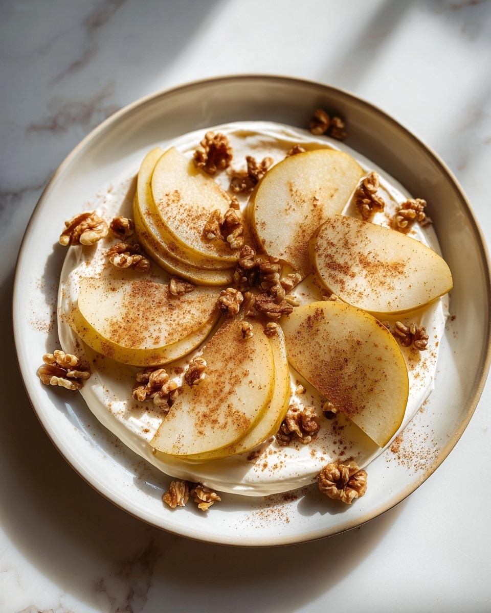The dish shows six thick wedges of cooked pear, arranged in a circular pattern on a white plate. The pears are golden yellow with some dark brown char marks, giving a slightly caramelized look. Underneath the pears is a creamy white yogurt or sauce layer spread across the plate. The top of the pears and yogurt is sprinkled with small chopped brown walnuts and a light dusting of dark cinnamon powder. The plate is set on a white marbled surface with soft sunlight coming from the left. photo taken with an iphone --ar 4:5 --v 7