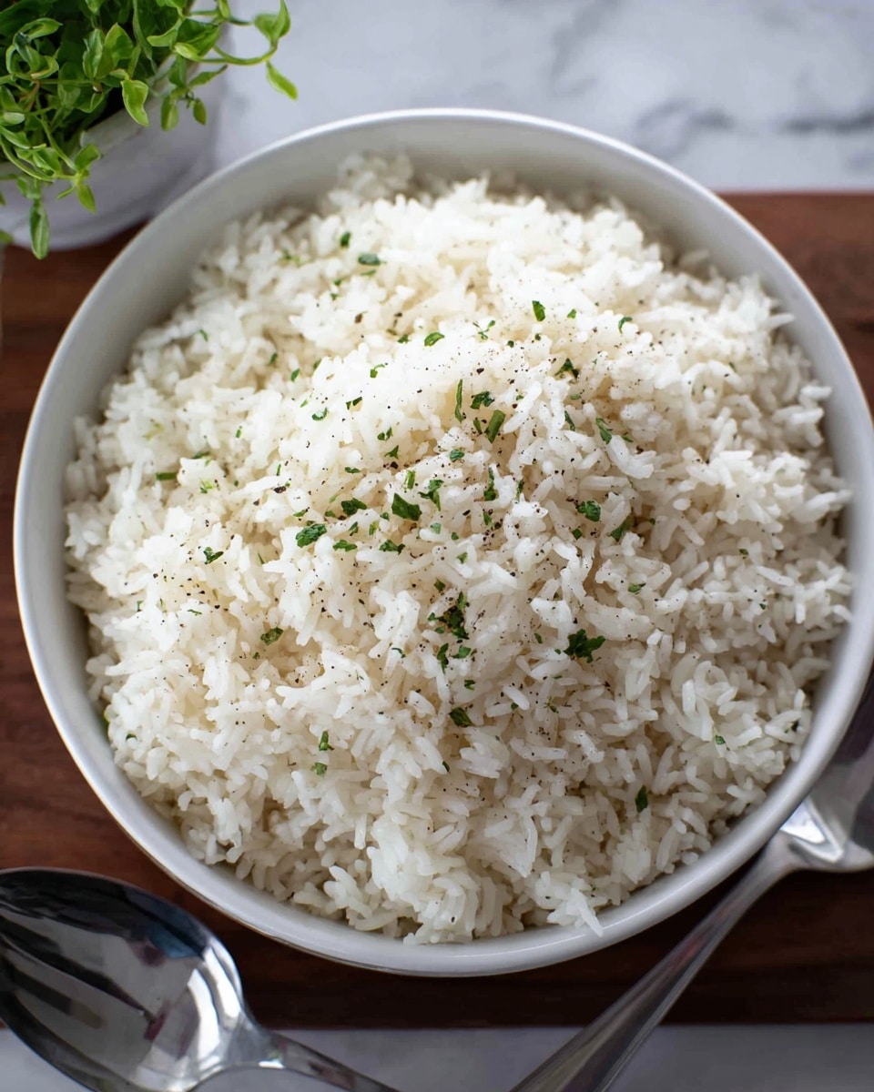 This image shows a close-up of a wooden spoon lifting a scoop of cooked white rice mixed with small green herb pieces. The rice grains are soft and slightly sticky, with a light, fluffy texture. The spoon is positioned over a large white bowl filled with more of the same herb-seasoned rice, which has a slightly glossy look from moisture. The background is blurred but looks like a white marbled surface. photo taken with an iphone --ar 4:5 --v 7