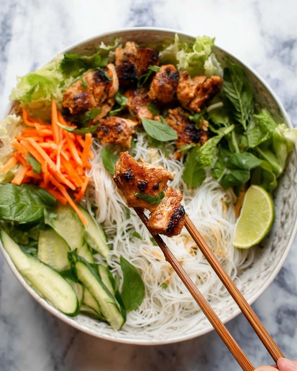 The image shows a white bowl filled with a colorful dish. The bottom layer has thin white rice noodles with a soft texture. On top of the noodles, there are golden-brown grilled chicken pieces with a slightly charred look. Around the noodles and chicken, there are fresh green herbs like cilantro and basil leaves, along with bright orange carrot sticks and green cucumber strips arranged in layers. A green lime wedge is placed on the side of the bowl. In the foreground, a pair of wooden chopsticks holds some grilled chicken and rice noodles. The whole bowl is set on a white marbled surface. photo taken with an iphone --ar 4:5 --v 7