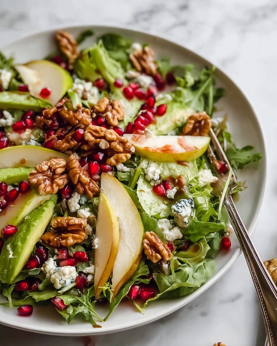 The dish shows a white bowl filled with a fresh salad that has three main layers: the bottom layer is a mix of leafy greens, mostly light and dark green lettuce leaves with a slightly rough texture; the middle layer contains scattered red pomegranate seeds and small chunks of white and blue-veined cheese; the top layer includes golden brown walnuts and thin, curved slices of green apple with light yellow flesh, all glistening with a shiny dressing. A silver fork rests inside the bowl, and the bowl is set on a white marbled surface with part of a halved pomegranate visible nearby. Photo taken with an iphone --ar 4:5 --v 7