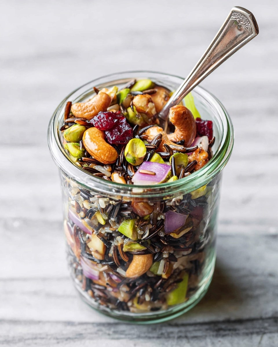 A clear glass bowl filled with a wild rice salad showing mixed layers of black wild rice, bright red dried cranberries, chunks of orange pecans, and small pieces of light green celery and purple red onion scattered throughout. A silver fork is digging into the salad from the right side. The bowl sits on a white marbled surface with a folded orange and white patterned cloth visible behind it. Photo taken with an iphone --ar 4:5 --v 7