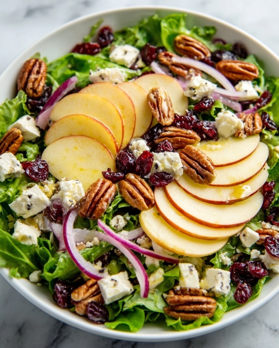 A large white bowl filled with a fresh salad sits on a white marbled surface. The salad has several layers: a bed of green arugula leaves at the bottom, topped with slices of red apple and pale yellow pear arranged evenly around the bowl. There are also dark red dried cranberries scattered across, and crunchy brown pecans sprinkled on top. Crumbled white cheese is spread over the salad, adding light contrast. Near the bowl, there is a jar of dressing and an apple, with a woman's hand holding a white fork on the side. photo taken with an iphone --ar 4:5 --v 7
