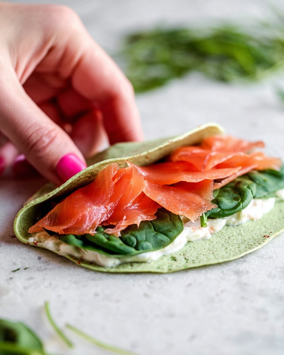 The image shows a wooden cutting board holding fourteen rolled pinwheel sandwiches arranged in a grid pattern. Each pinwheel has three visible layers: the outer layer is a green spinach tortilla wrap with a soft texture, the middle layer is a creamy white spread, and the inner layer is a vibrant red slice of smoked salmon. The sandwiches are tightly rolled and sliced evenly, showing clear spirals of the three layers. A few sandwiches lie on a white marbled surface near the cutting board, along with scattered small green herb pieces, adding a fresh touch. photo taken with an iphone --ar 4:5 --v 7