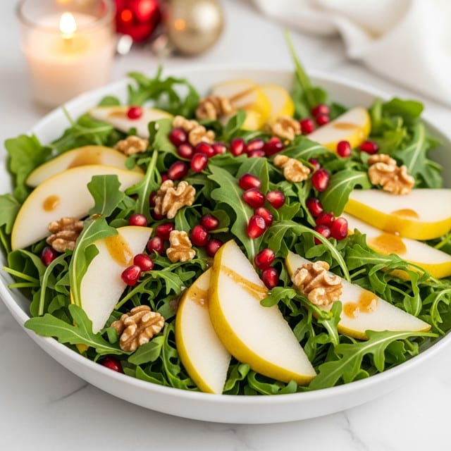 A fresh salad in a white bowl filled with layers of green arugula leaves forming the base, topped with scattered bright red pomegranate seeds adding a pop of color, chunks of yellow pear slices placed evenly around the salad, and crunchy walnut pieces sprinkled on top. The salad is on a white marbled surface with warm, soft lighting that highlights the freshness and texture of the ingredients. A small candle and festive ornaments are visible softly blurred in the background. Photo taken with an iphone --ar 4:5 --v 7