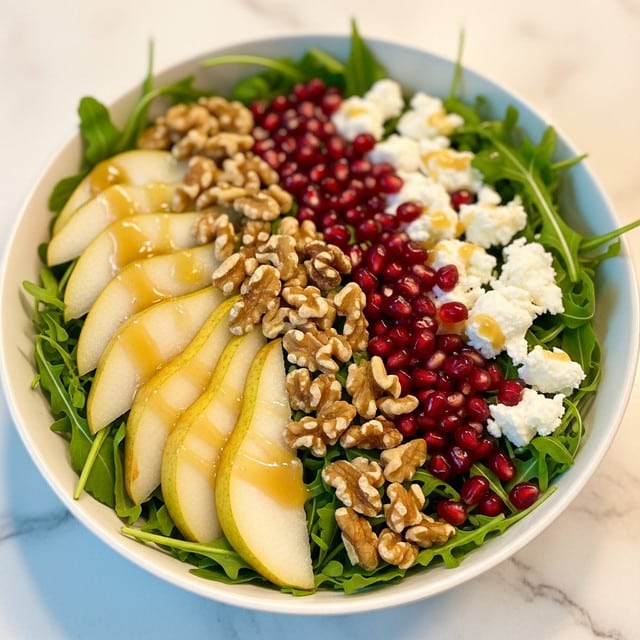 A white bowl filled with a fresh salad placed on a white marbled surface, showing layers that include bright green arugula leaves as the base, topped with golden sliced pears arranged around the side, scattered walnut pieces adding a rough texture, small shiny red pomegranate seeds spread over for a pop of color, and creamy pieces of soft cheese placed lightly on top. The lighting is warm and soft, giving the salad a fresh and inviting look. Photo taken with an iphone --ar 4:5 --v 7