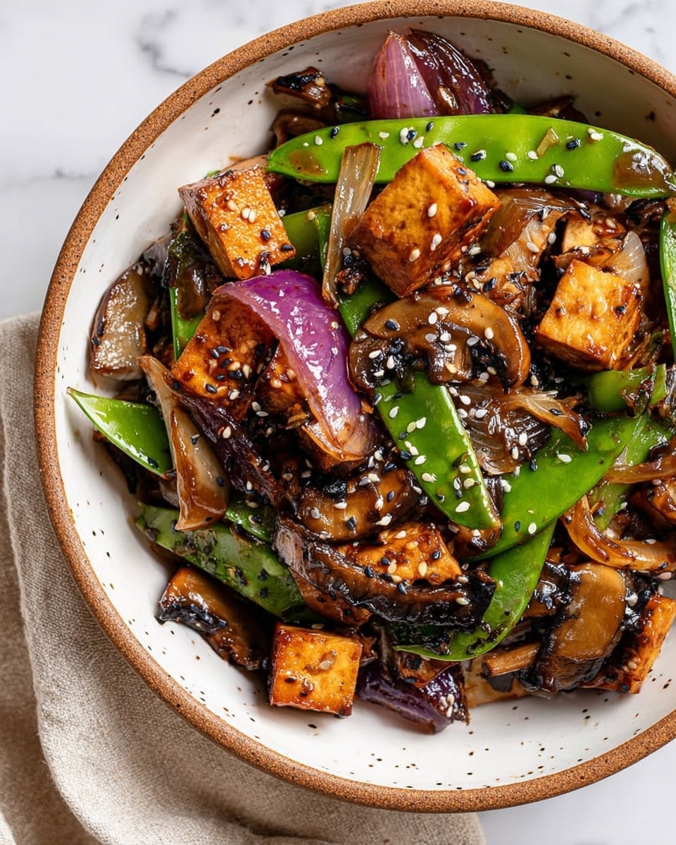 A close-up view of a bowl filled with a colorful stir-fry dish, layered with golden-brown tofu cubes, bright green snap peas, and sautéed sliced mushrooms that have a soft, glossy texture. Mixed among these are caramelized pieces of red onion adding a deep purple color and slight shine. The dish is topped with a scattering of black and white sesame seeds, adding a crunchy texture. The bowl is white with small brown speckles and a brown rim, resting on a white marbled surface next to a light beige cloth. The overall look is fresh and vibrant with a glossy sauce coating the ingredients, photo taken with an iphone --ar 4:5 --v 7