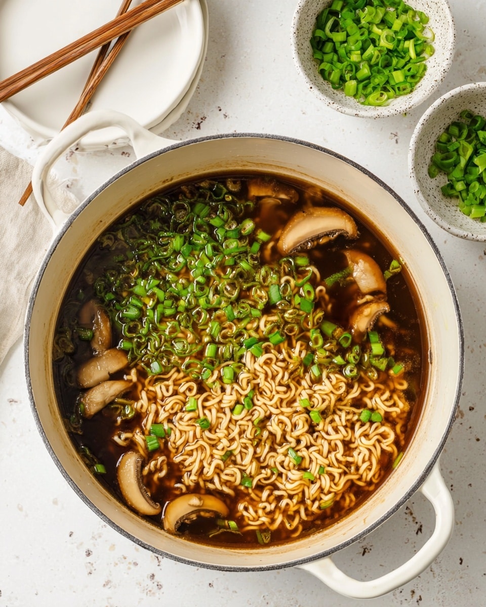 A large white pot filled with dark brown broth contains wavy light brown ramen noodles floating in the middle layer, and several pale tan mushroom slices scattered throughout. Bright green chopped scallions are spread generously on the top layer, covering the broth's surface. To the top right of the pot, there are small stacked white speckled bowls filled with more chopped green scallions, all placed on a white marbled surface. At the top left corner, part of a white plate with light brown wooden chopsticks resting on it is visible. Photo taken with an iphone --ar 4:5 --v 7
