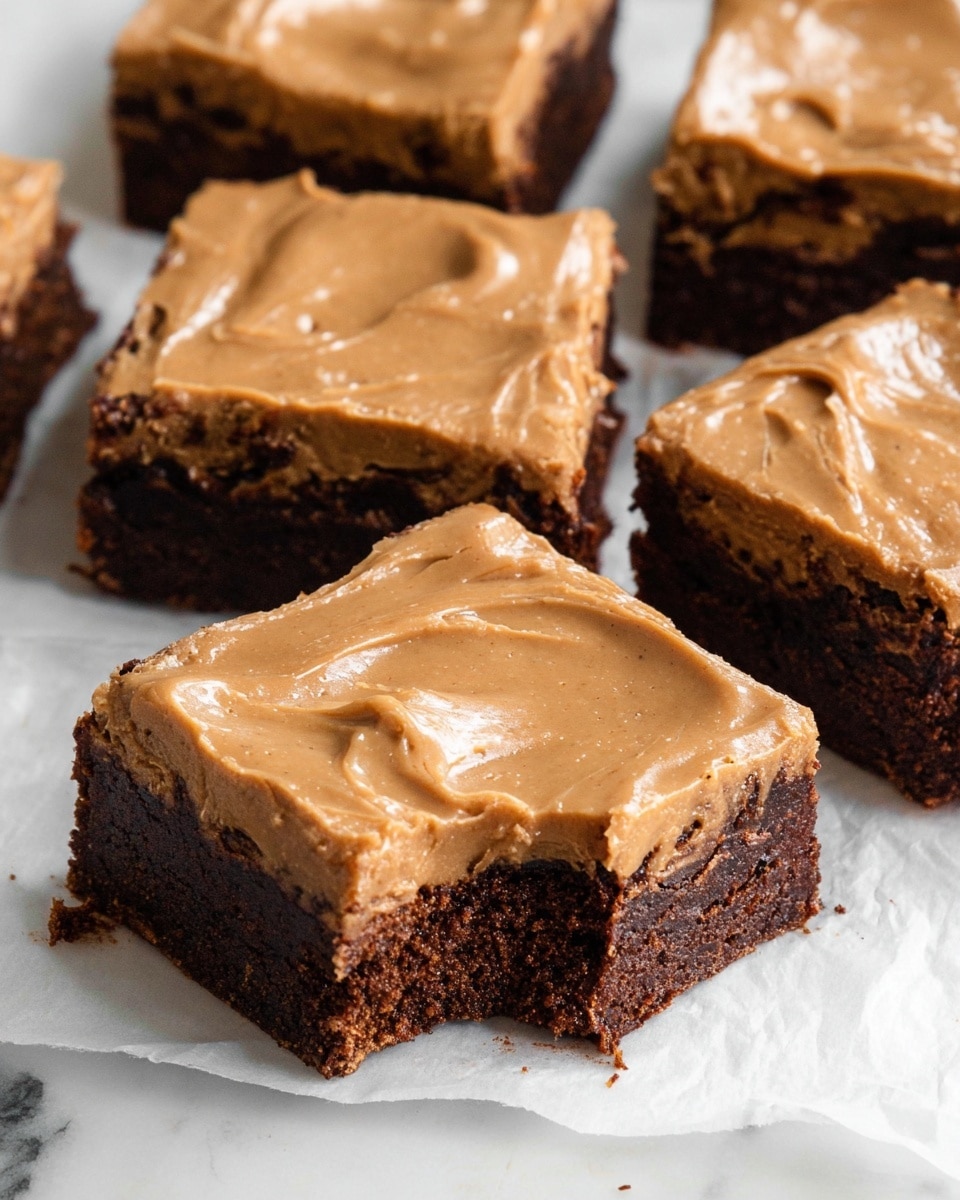 The image shows a close-up of a white rectangular baking dish filled with a smooth, thick light brown batter that has a creamy texture with swirled patterns on top, likely indicating a mix of ingredients or flavor swirls. Darker brown streaks are scattered unevenly throughout the batter, adding contrast to the lighter brown base. The dish is placed on a soft white linen cloth, all set against a white marbled surface. Photo taken with an iphone --ar 4:5 --v 7