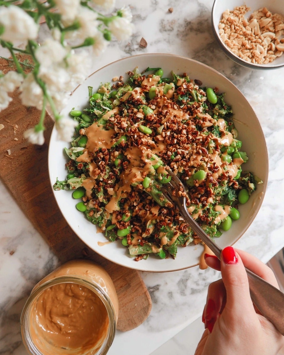 A close-up of a bowl filled with a colorful mixed salad made of green leafy vegetables, edamame beans, chopped nuts, and grilled pieces, topped with a creamy light brown sauce drizzled unevenly across the salad. A spoon with the sauce covered is placed inside a jar next to the bowl, and a woman's hand holding a fork with red nail polish is about to take some salad. The bowl is light peach colored, sitting on a wooden surface, with a white marbled texture background, and white flowers and a white cup with black spots are visible in the background. photo taken with an iphone --ar 4:5 --v 7