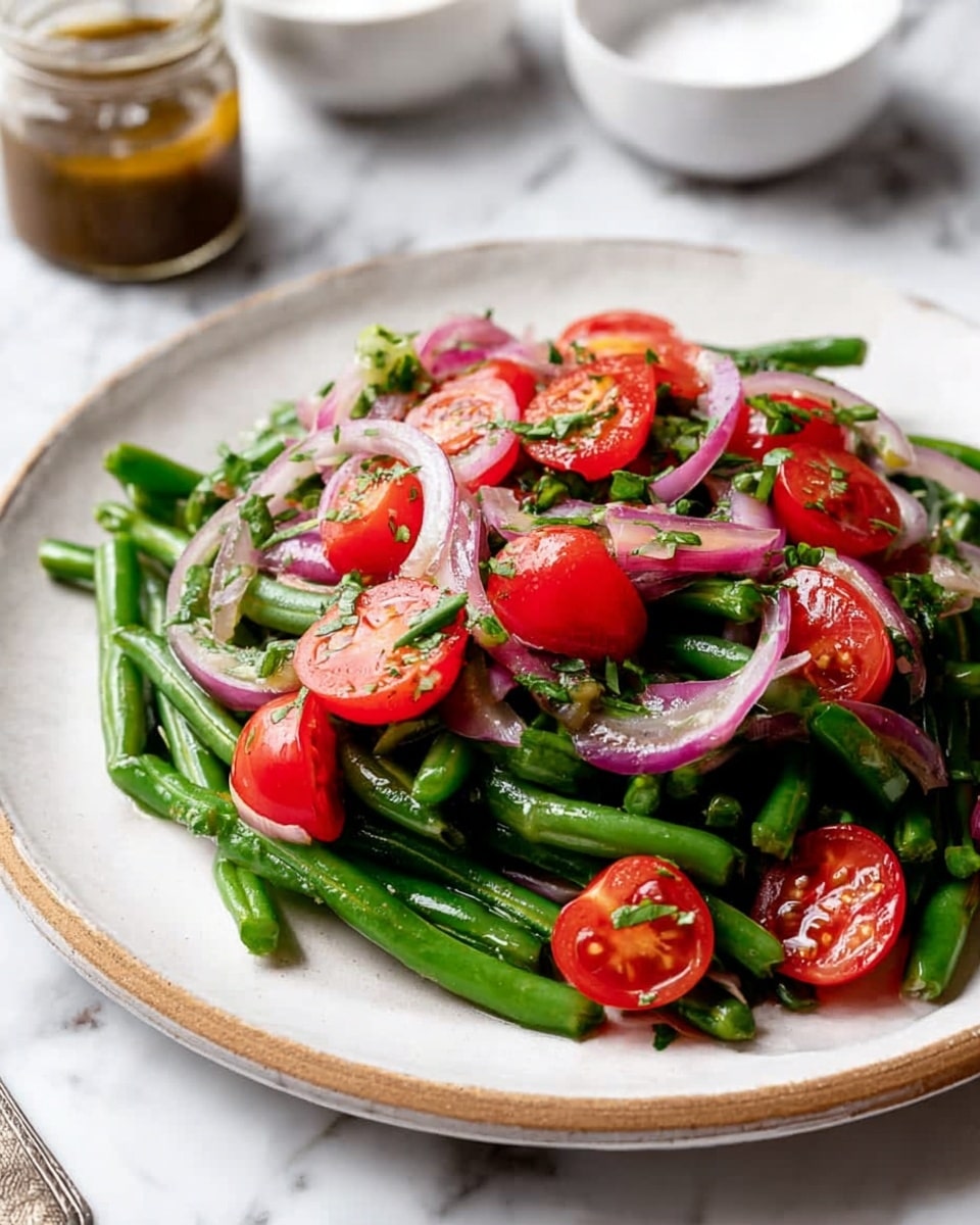 A white plate holds a fresh salad made of three main layers: at the bottom, bright green, slightly shiny asparagus pieces cut into medium lengths; the middle layer consists of vibrant red cherry tomato halves, scattered evenly; on top, thin slices of pale purple onion rings are mixed throughout, along with chopped dark green leafy herbs. The textures are crisp and fresh, with a slight shine from a light dressing. Two vintage silver spoons rest on each side of the plate. The scene is set on a white marbled surface with a small glass jar of dressing and a white bowl with pepper in the background. Photo taken with an iphone --ar 4:5 --v 7