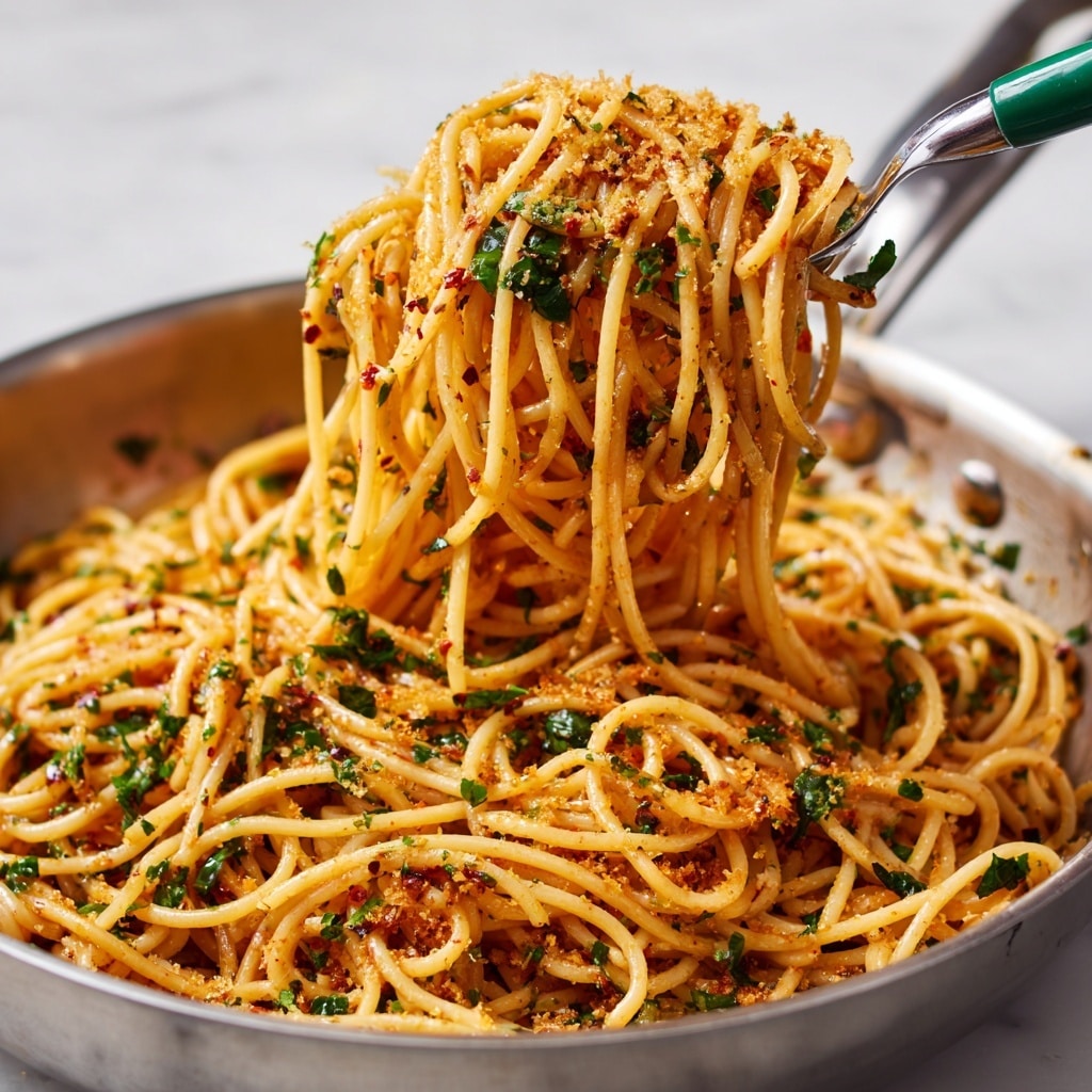 A close-up of a pan filled with spaghetti noodles mixed with green herbs and red pepper flakes, topped with a sprinkle of golden toasted crumbs. The spaghetti is lifted by a utensil with a green handle, showing the noodles tangled tightly with visible seasoning. The noodles have a light orange tint from the sauce, and the pan sits on a white marbled texture surface. photo taken with an iphone --ar 4:5 --v 7