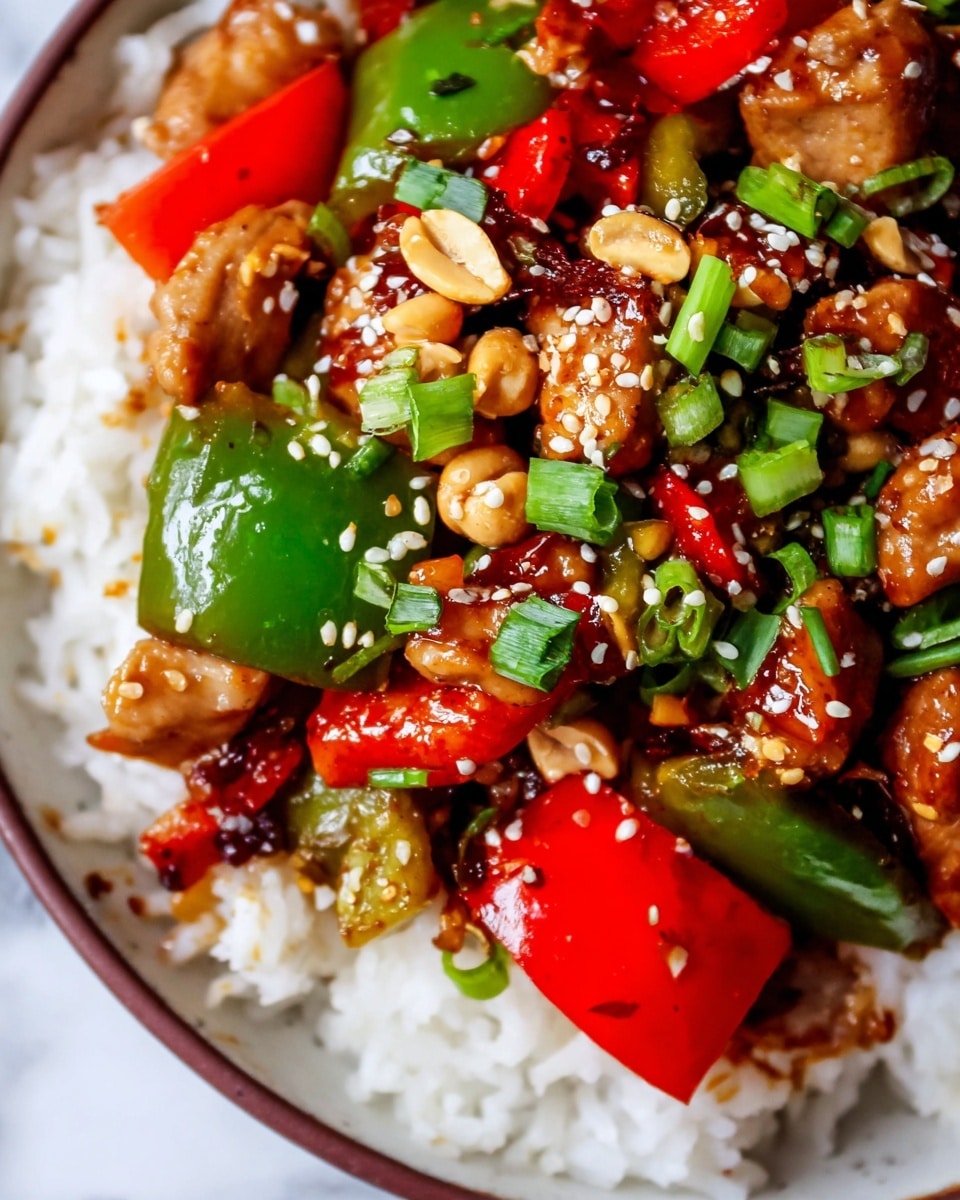 This image shows a close-up of a cooked dish in a black cast-iron pan placed on a white marbled surface. The dish has several layers: at the base, there are browned, bite-sized pieces of chicken with a crispy texture, mixed with chunks of bright red bell peppers and glossy green zucchini pieces. There are also visible pieces of cooked green bell peppers and sliced green onions scattered throughout. Small whole peanuts are mixed in, adding a crunchy texture. To the side of the pan, there are fresh orange slices with a vibrant orange color. The colors in the dish are warm and vivid, with a shiny glaze coating the ingredients. photo taken with an iphone --ar 4:5 --v 7