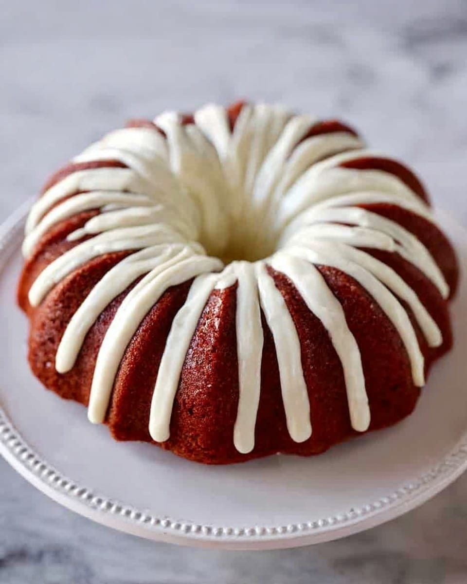 The image shows a round bundt cake with a reddish-brown color on a white plate. The cake has thick, creamy white icing evenly spread in long strips radiating from the center top of the cake to the edges, forming a symmetrical pattern. The smooth texture of the icing contrasts with the slightly rough surface of the cake. The white plate has a subtle decorative edge and is placed on a white marbled surface. Photo taken with an iphone --ar 4:5 --v 7