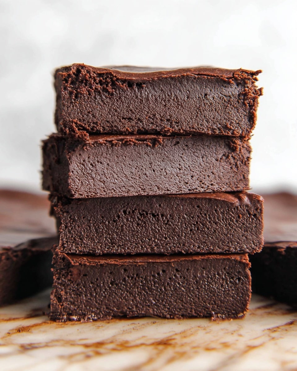The image shows a stack of four thick, rich chocolate brownies with a dense, moist texture and a slightly rough surface. Each brownie has a dark brown color with a smooth, matte top layer that looks slightly cracked. The stack sits on a black cooling rack placed on a white marbled surface, with more brownies blurred in the background. Photo taken with an iphone --ar 4:5 --v 7