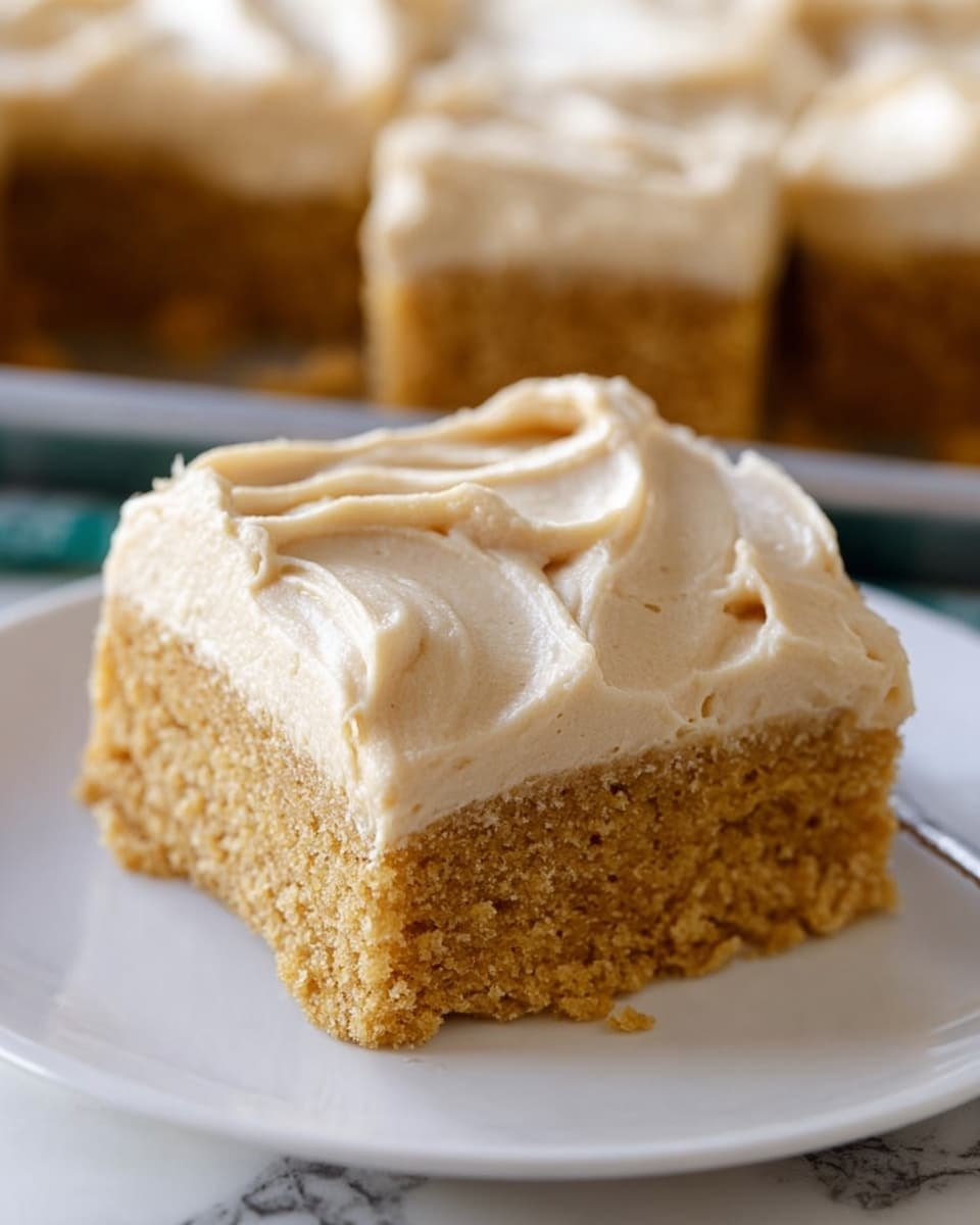 A close-up view of a square slice of cake with two layers on a white plate, placed near a larger baking tray with the rest of the cake that has a thick light tan frosting spread smoothly on top. The cake’s bottom layer is a light golden brown with a crumbly texture, while the top layer is a thick, creamy light tan frosting with a slightly swirled pattern. The baking tray rests on a blue and white checkered cloth over a white marbled surface. A metal spatula slightly lifts one slice from the tray, showing the frosting and cake layers clearly. Photo taken with an iphone --ar 4:5 --v 7