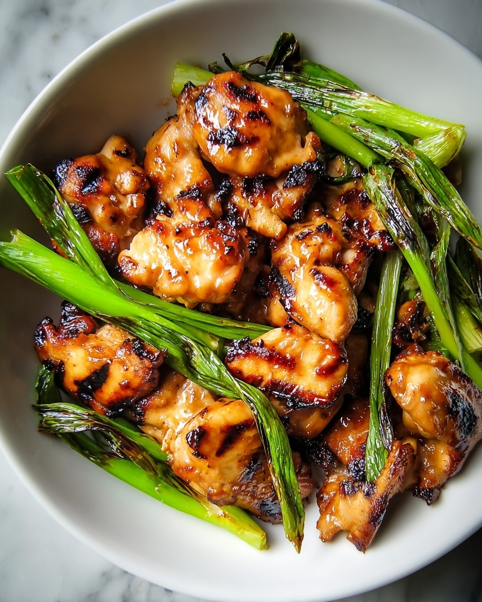 The image shows a white bowl filled with grilled chicken pieces that have a shiny, golden-brown glaze with dark char marks. The chicken pieces are layered closely, each having a slightly irregular shape with a glossy texture. Around and between the chicken pieces are bright green grilled scallions with some parts charred, adding a fresh pop of color and texture contrast. The chicken and scallions fill the bowl nearly to the edge, placed on a white marbled surface. photo taken with an iphone --ar 4:5 --v 7