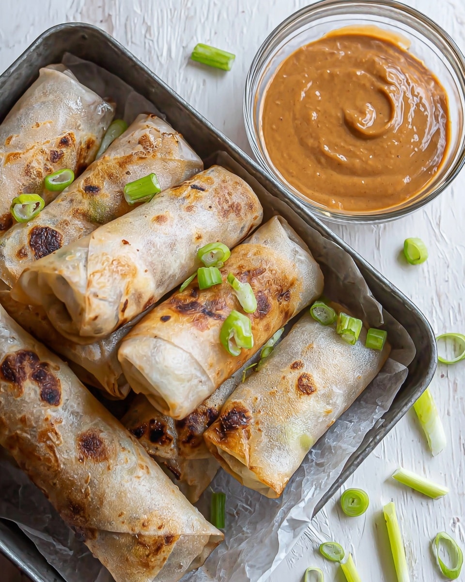 The image shows several spring rolls with a thin, lightly browned and slightly crispy outer layer that appears almost translucent, revealing colorful vegetable filling inside. The filling shows layers of orange, green, and light yellow vegetables, peeking out from the open end of one roll. The spring rolls are placed close together on a white marbled surface with a few small green onion slices scattered around. To the right, there is a clear glass bowl containing a smooth, light brown dipping sauce. The surface beneath the food has a crinkled texture, with the rolls slightly shiny from oil used in cooking. Photo taken with an iphone --ar 4:5 --v 7