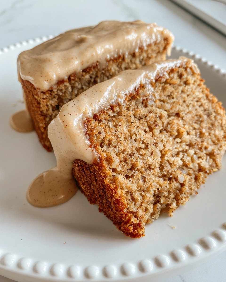 The image shows two slices of moist, crumbly cake with a light brown color, placed side by side on a white plate. Each slice has one visible layer of cake, topped with a thick layer of creamy, light beige frosting that has a smooth texture and specks of spice. The frosting is spread across the top of the cake and drips slightly down the sides, with some pooling around the base. The white plate rests on a white marbled texture surface. photo taken with an iphone --ar 4:5 --v 7