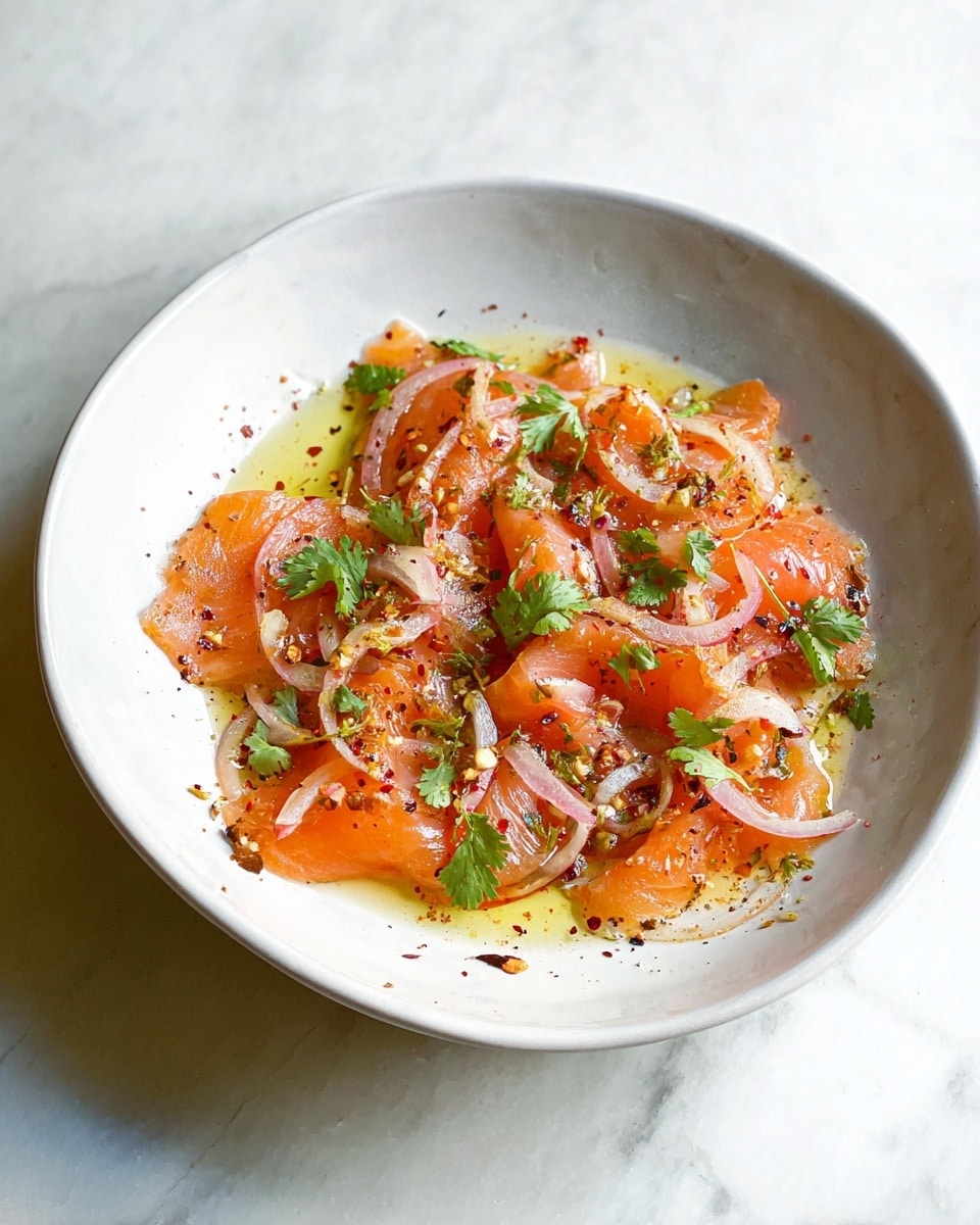 A white bowl on a white marbled surface holds thin slices of bright orange salmon, slightly curled and layered loosely. The salmon is topped with small, light pink rings of shallots scattered evenly across the dish. Bright green cilantro leaves are spread on top, adding fresh color contrast. The entire dish is lightly drizzled with golden olive oil, giving it a shiny texture, and sprinkled with coarse black pepper and red pepper flakes, adding specks of dark and red. photo taken with an iphone --ar 4:5 --v 7