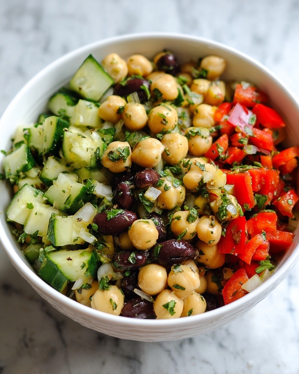 A white bowl filled with a colorful chickpea salad that has three main layers: the bottom layer is creamy beige chickpeas, the middle layer has bright red bell pepper pieces and dark brown black beans, and the top layer shows fresh green cucumber chunks mixed with finely chopped green herbs and small bits of cooked onion. The salad looks fresh and shiny with a light dressing. The bowl sits on a white marbled surface. photo taken with an iphone --ar 4:5 --v 7
