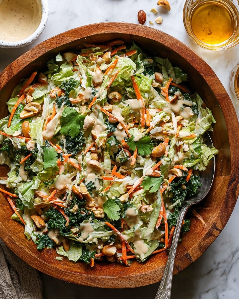 A large wooden bowl filled with a colorful salad that has several layers; the bottom layer is light green chopped lettuce, followed by shredded orange carrots and shredded white chicken pieces scattered throughout. On top, there are chopped green herbs and whole cashew nuts, all covered with a light tan creamy dressing drizzled unevenly. Around the bowl, there is a small white plate with a beige creamy sauce on the left and a glass cup with a golden liquid on the right, all set on a white marbled surface. photo taken with an iphone --ar 4:5 --v 7